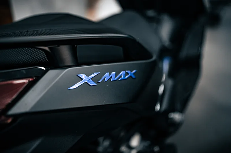 Logotipo XMAX em relevo na carenagem lateral da scooter.